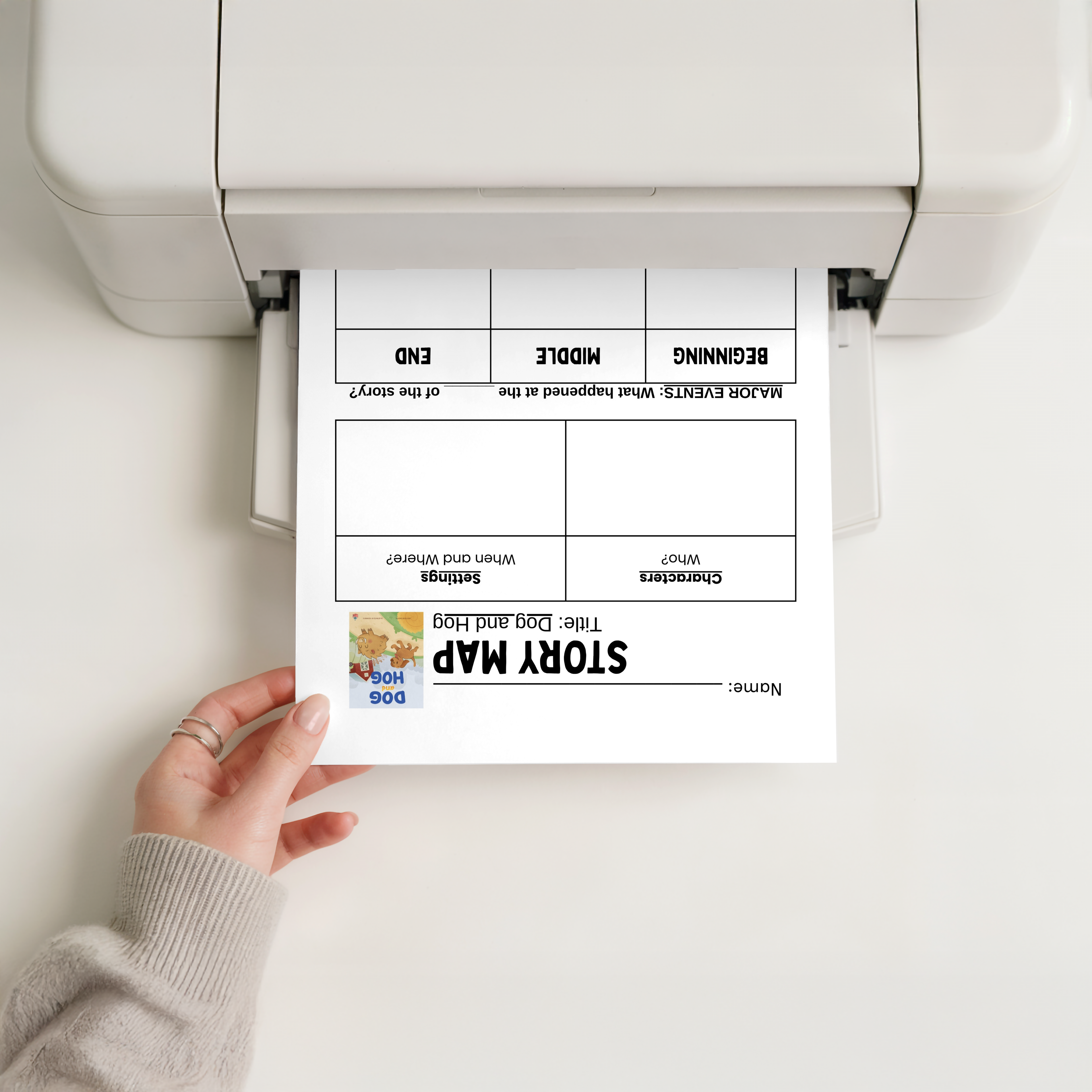 Hand holding a printed story map template in front of a printer.