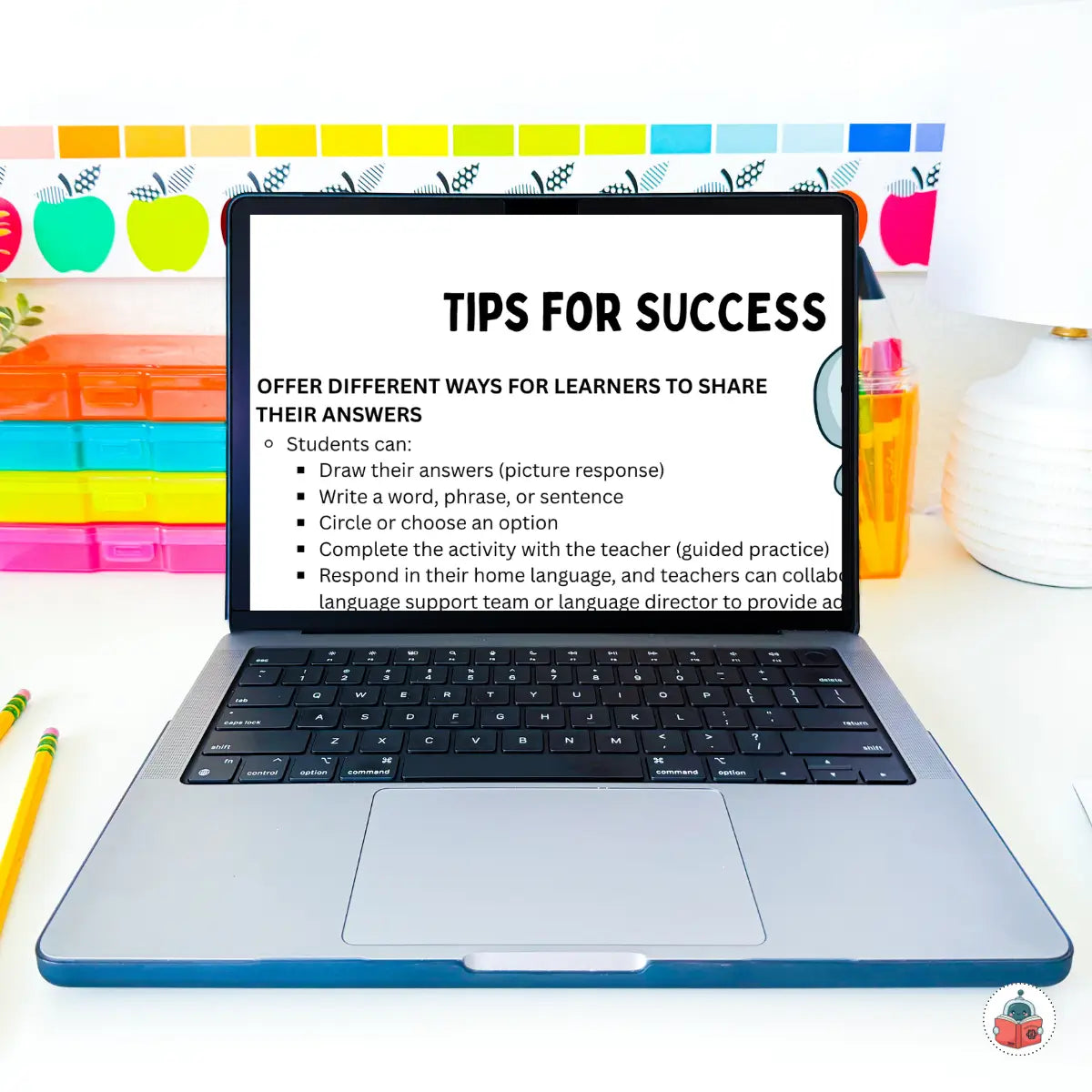An open silver laptop on a white desk displaying a digital slide titled 'TIPS FOR SUCCESS' about learner answer sharing methods. The background shows colorful school-themed wall decorations, including apple cutouts and a chalkboard marker, with pencils on both sides.