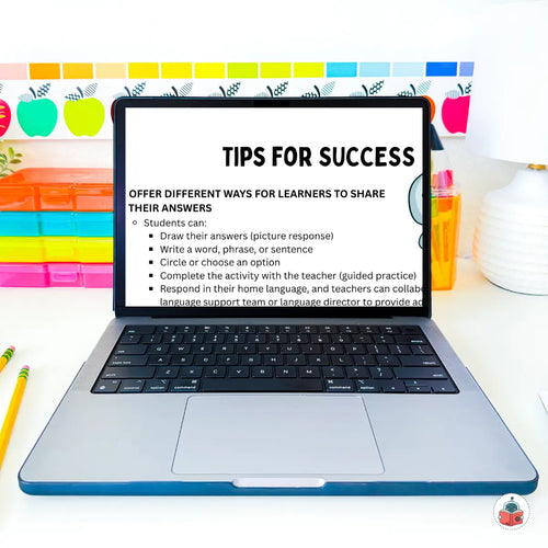 An open silver laptop on a white desk displaying a digital slide titled 'TIPS FOR SUCCESS' about learner answer sharing methods. The background shows colorful school-themed wall decorations, including apple cutouts and a chalkboard marker, with pencils on both sides.